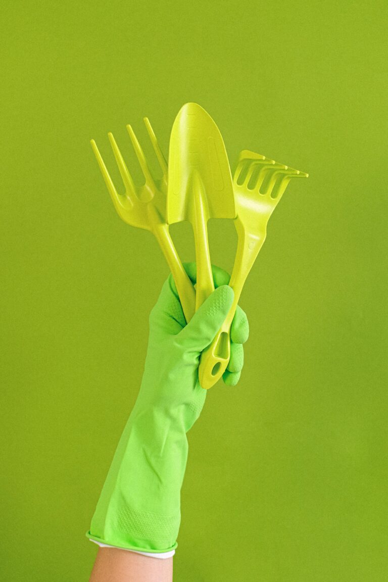 A gloved hand holding a garden trowel and hand rake